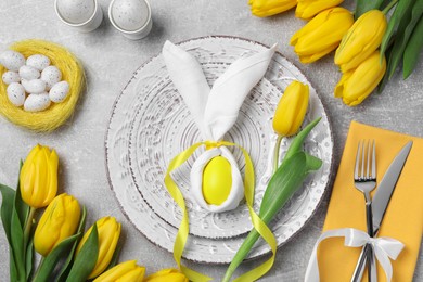 Photo of Festive table setting with bunny made of painted egg and napkin on light grey background, flat lay. Easter celebration