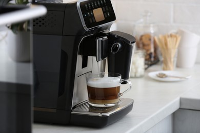 Modern electric espresso machine making coffee with milk on white marble countertop in kitchen