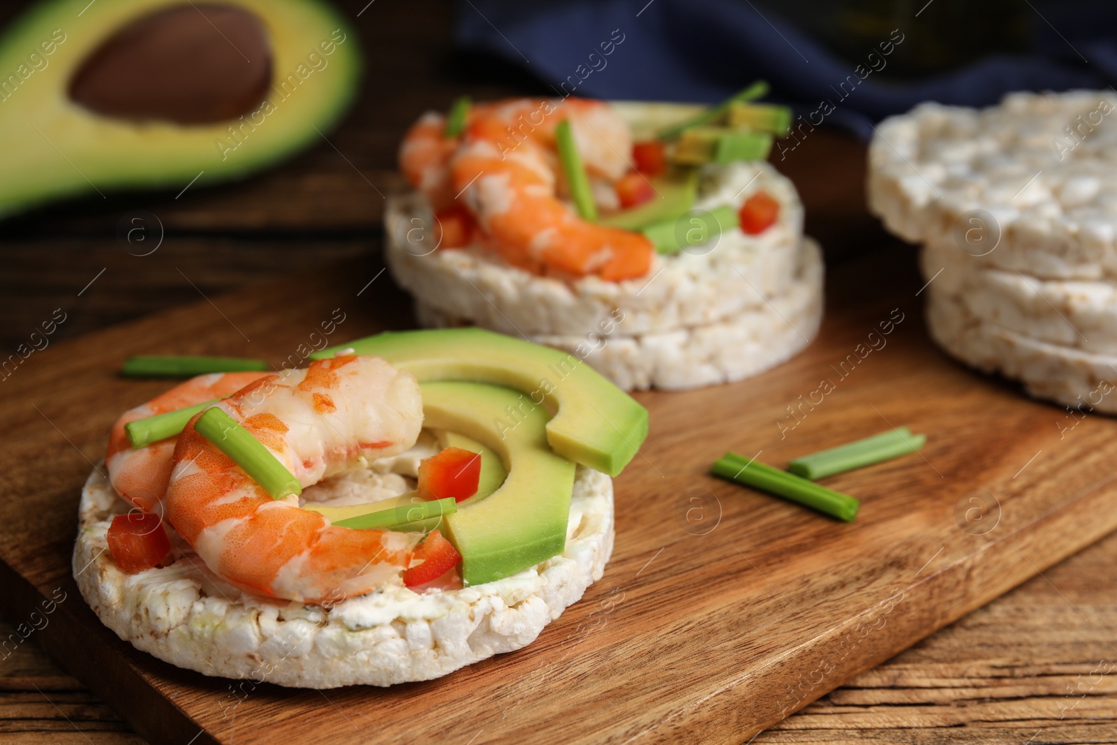 Photo of Puffed rice cakes with shrimps and avocado on wooden board, closeup