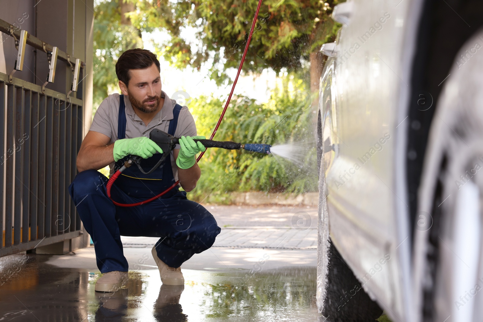 Photo of Worker washing auto with high pressure water jet at outdoor car wash