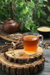 Photo of Aromatic licorice tea in cup and dried sticks of licorice root on black wooden table, space for text
