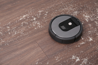 Photo of Removing groats from wooden floor with robotic vacuum cleaner at home. Space for text