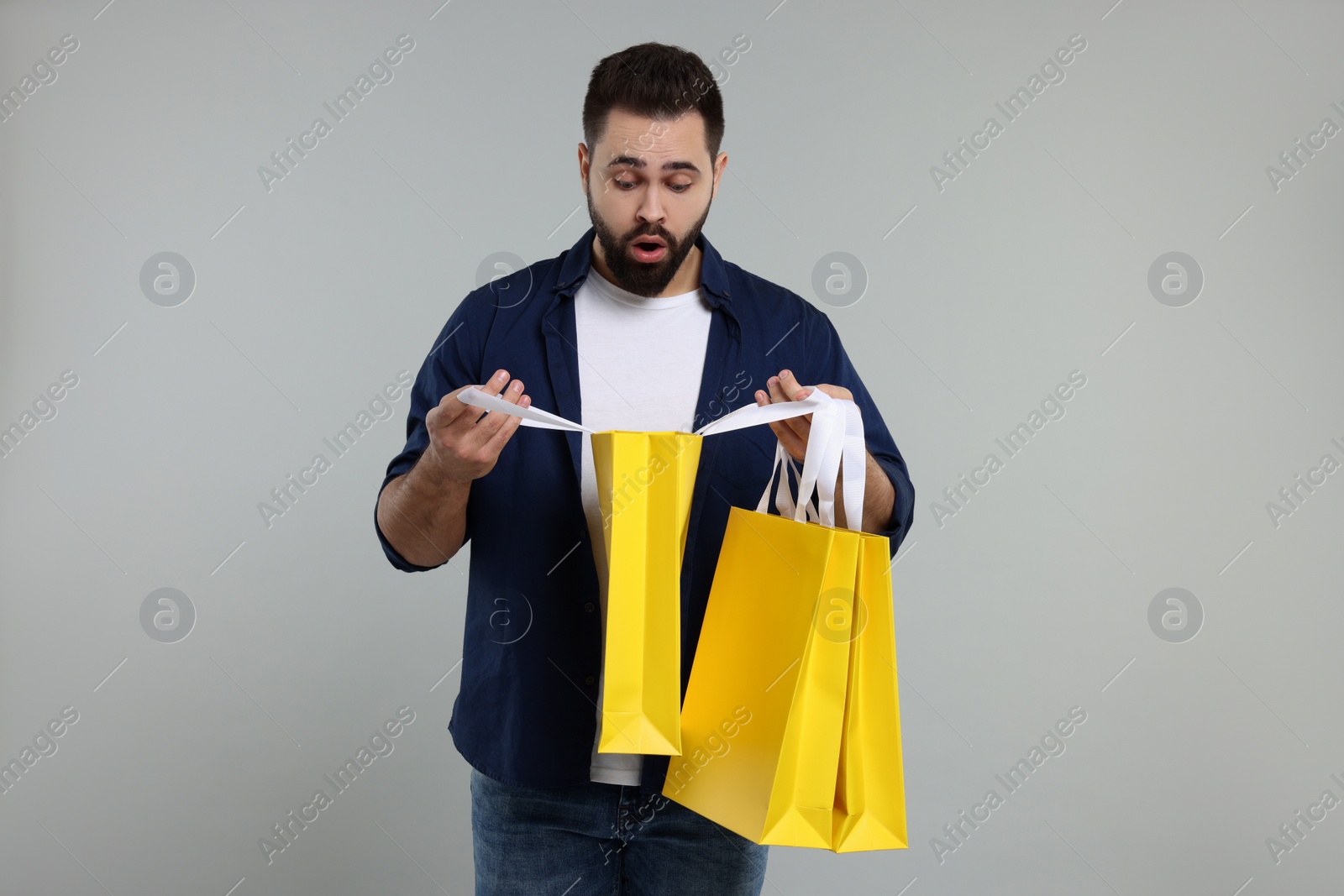 Photo of Surprised man with shopping bags on grey background