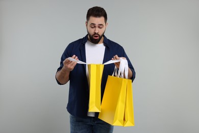 Surprised man with shopping bags on grey background