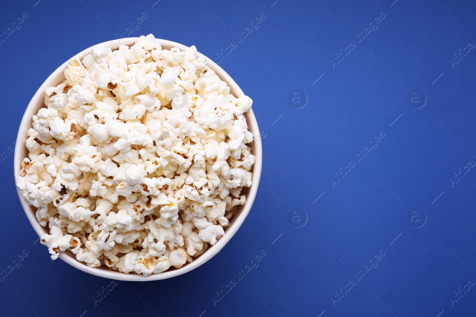 Photo of Bucket of tasty popcorn on blue background, top view. Space for text