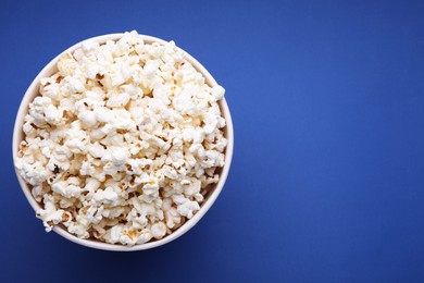 Bucket of tasty popcorn on blue background, top view. Space for text