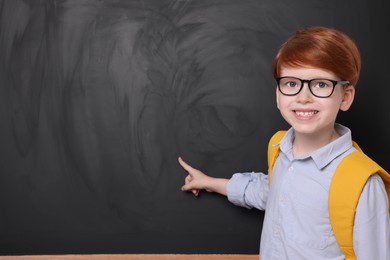 Photo of Smiling schoolboy in glasses pointing at something on blackboard. Space for text