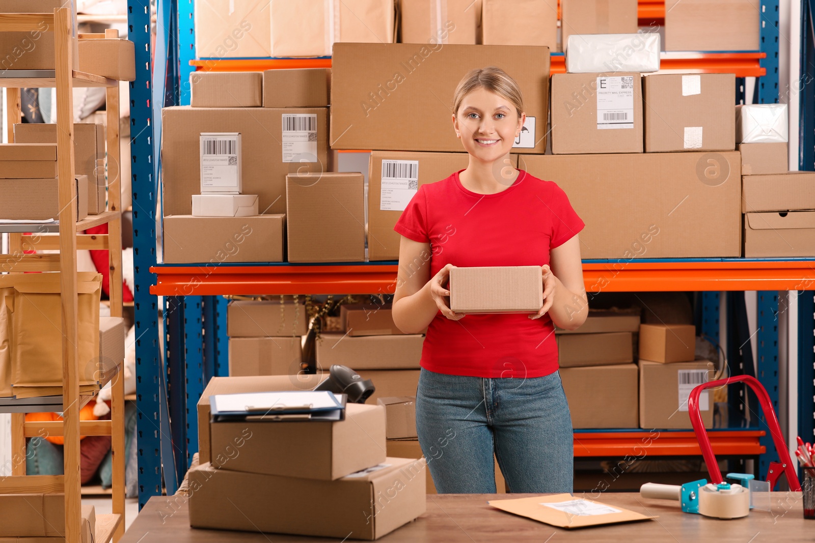 Photo of Post office worker with parcel near rack indoors