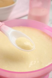 Spoon of healthy baby food over bowl, closeup