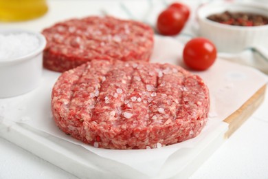 Photo of Raw hamburger patty with salt on white table, closeup