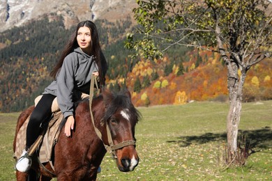Photo of Young woman riding horse in mountains on sunny day. Beautiful pet