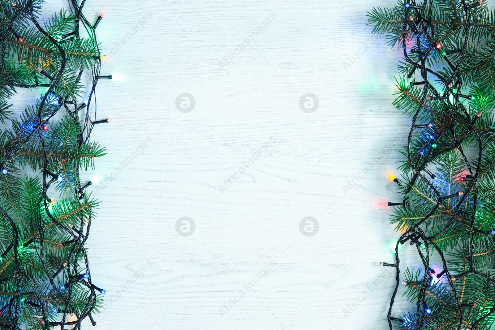 Photo of Glowing Christmas lights and fir branches on wooden background, top view