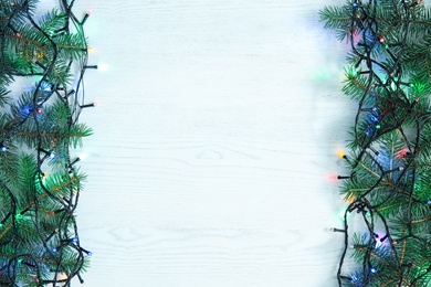 Glowing Christmas lights and fir branches on wooden background, top view