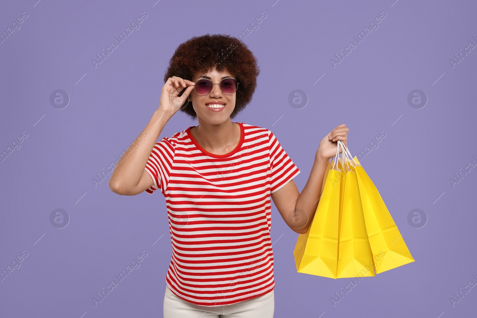 Photo of Happy young woman in stylish sunglasses with shopping bags on purple background