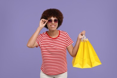Photo of Happy young woman in stylish sunglasses with shopping bags on purple background