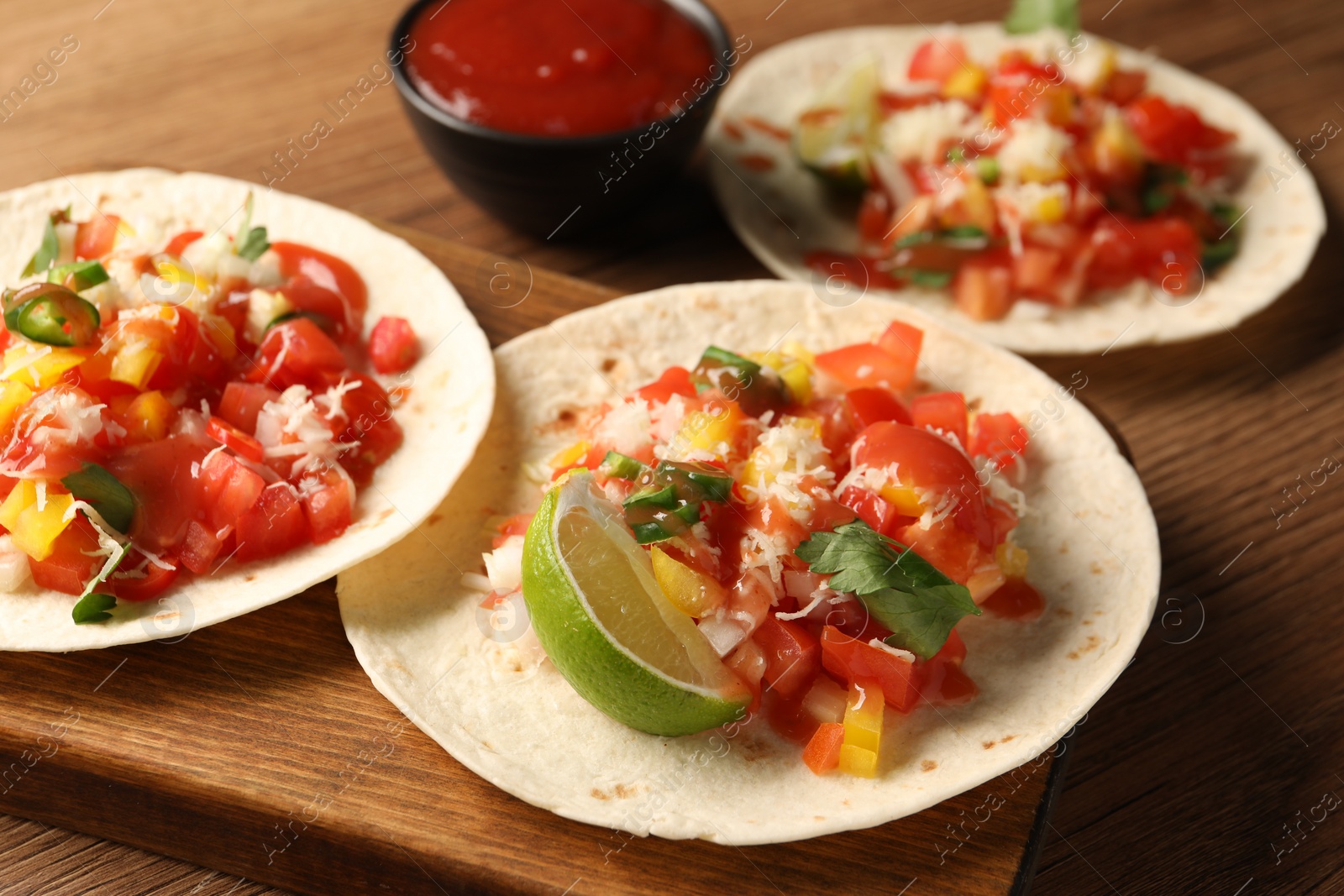 Photo of Delicious tacos with vegetables, lime and ketchup on wooden table, closeup