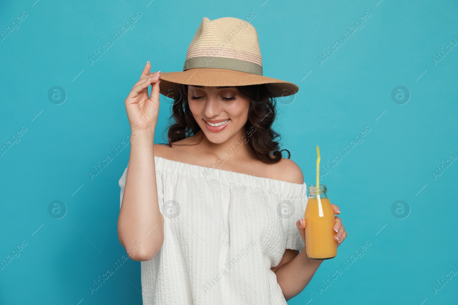 Photo of Beautiful young woman with straw hat and bottle of refreshing drink on light blue background