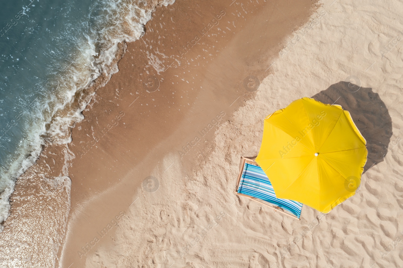 Image of Yellow beach umbrella and sunbed on sandy coast near sea, aerial view. Space for text