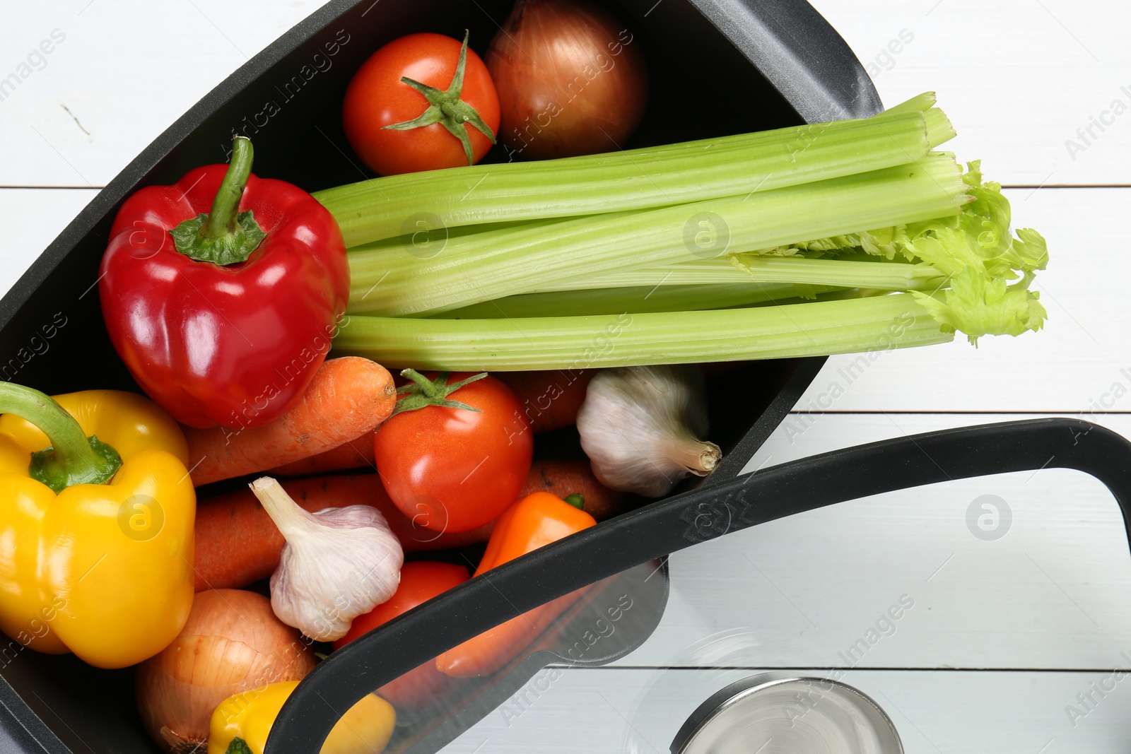 Photo of Black pot with fresh vegetables and glass lid on white wooden table, top view