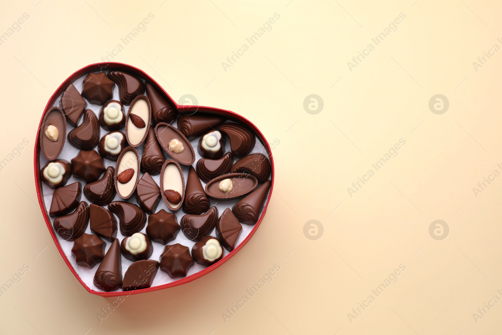 Photo of Heart shaped box with delicious chocolate candies on beige background, top view. Space for text