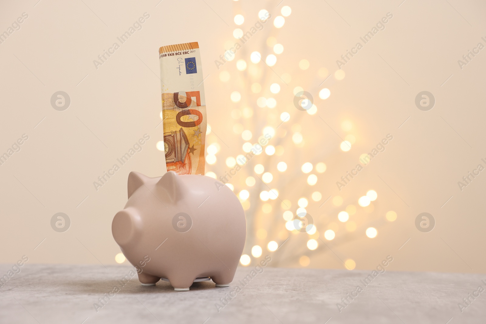 Photo of Piggy bank with euro banknote on grey table against blurred lights, space for text