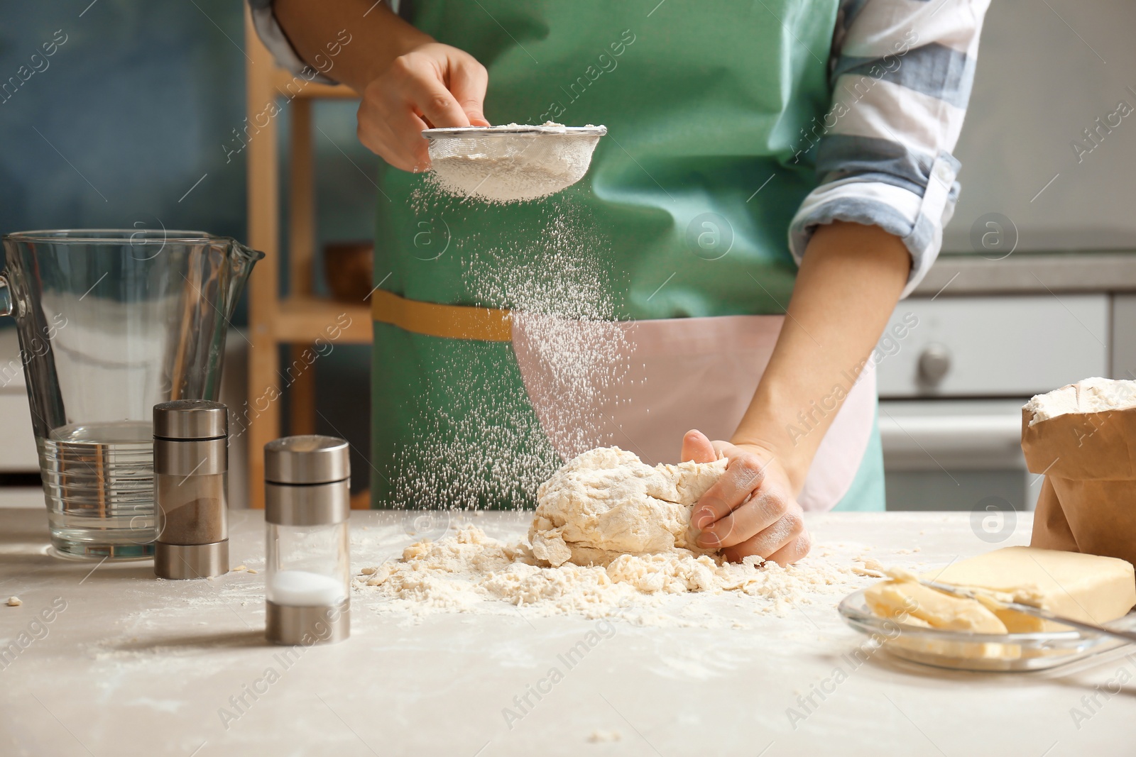 Photo of Woman sprinkling flour over dough on table in kitchen