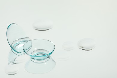 Photo of Contact lenses and drops of water on white reflective surface. Space for text