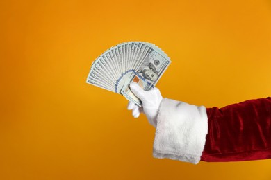 Photo of Santa holding dollar bills on orange background, closeup