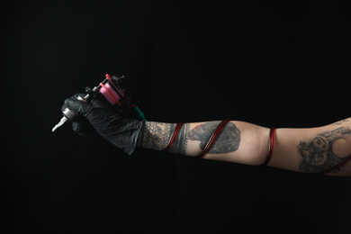 Tattoo artist with professional machine on black background, closeup