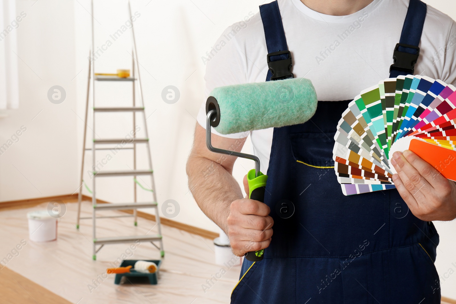 Photo of Male decorator with paint roller and color palette samples in empty room, closeup. Space for text