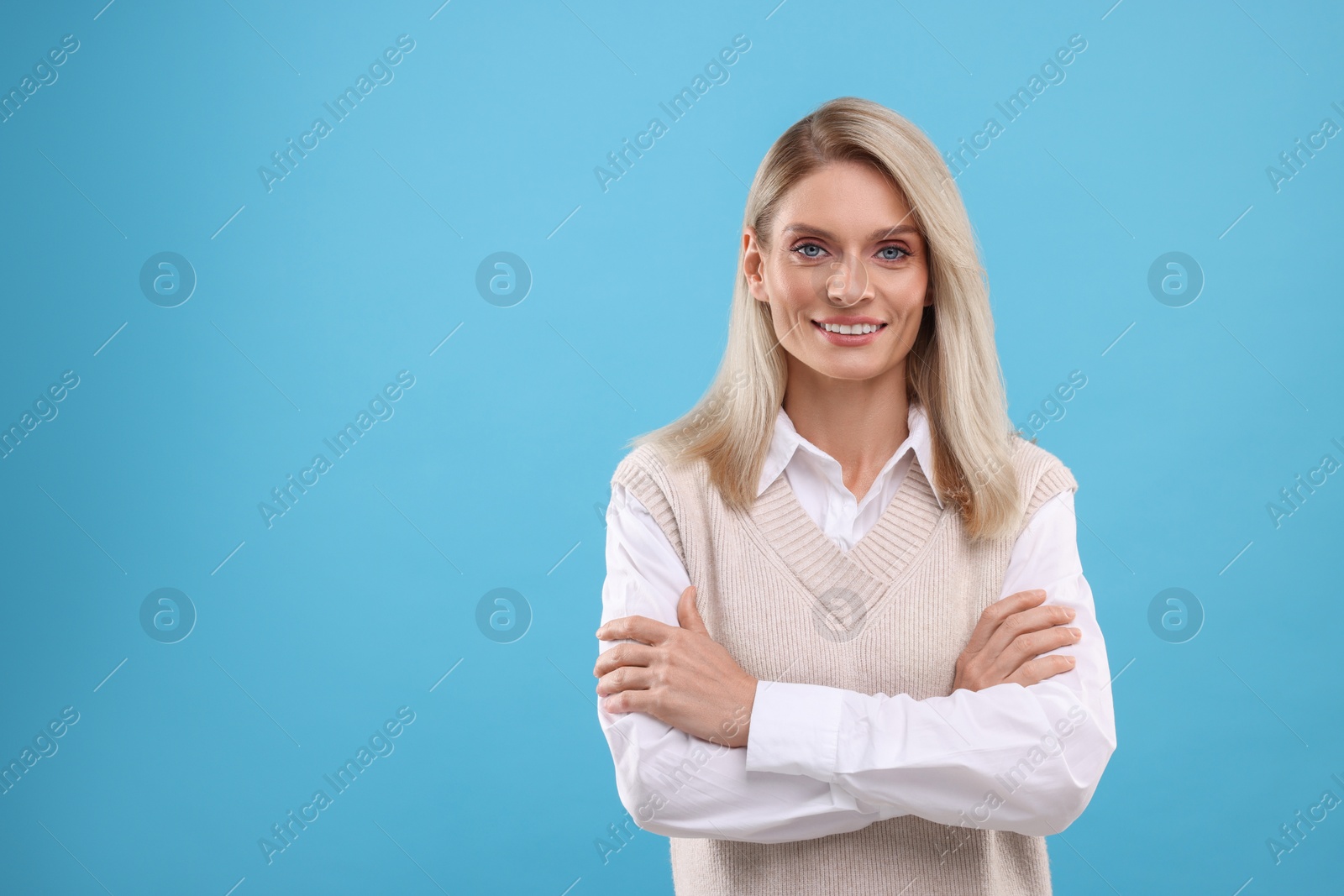 Photo of Portrait of smiling middle aged woman with crossed arms on light blue background. Space for text