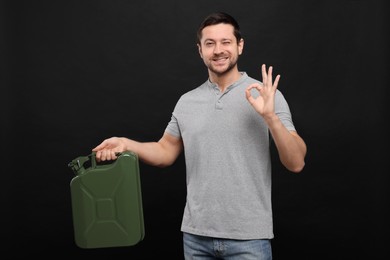 Man holding khaki metal canister and showing OK gesture on black background