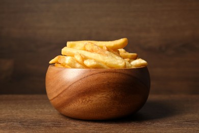 Photo of Delicious fresh french fries in bowl on wooden table, closeup