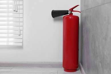 Photo of Red fire extinguisher on floor in corner, space for text