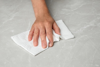 Woman wiping marble table with paper towel, closeup