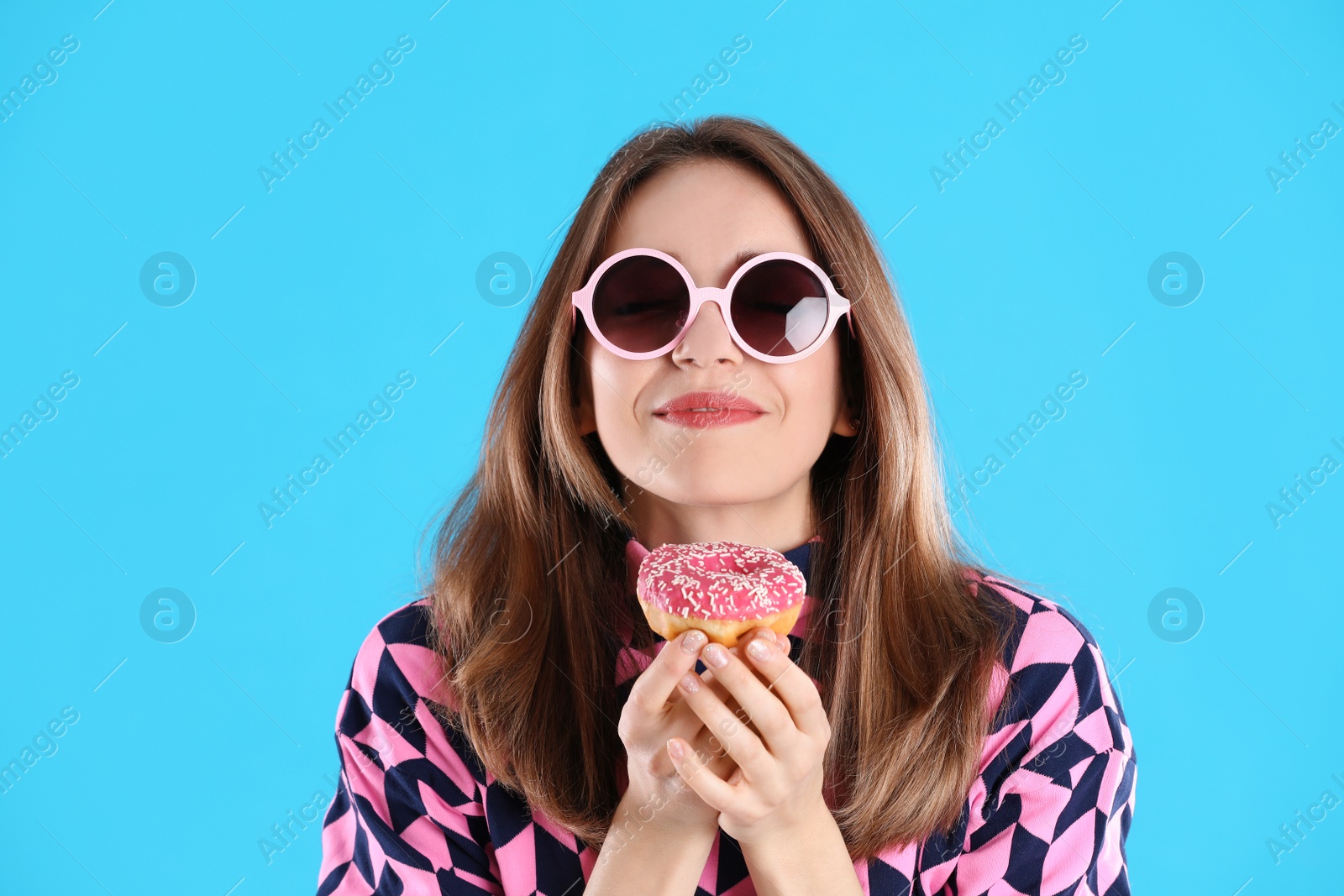 Photo of Beautiful young woman wearing sunglasses with donut on light blue background