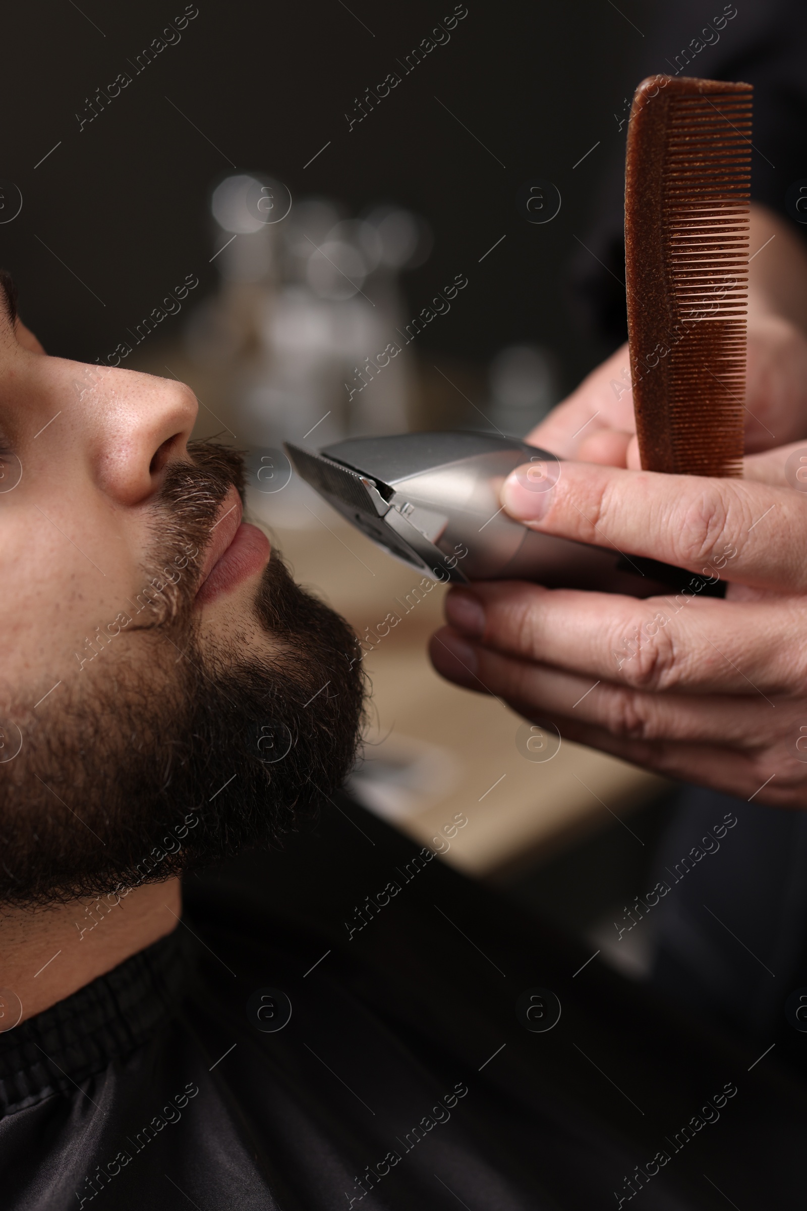 Photo of Professional barber trimming client's mustache in barbershop, closeup