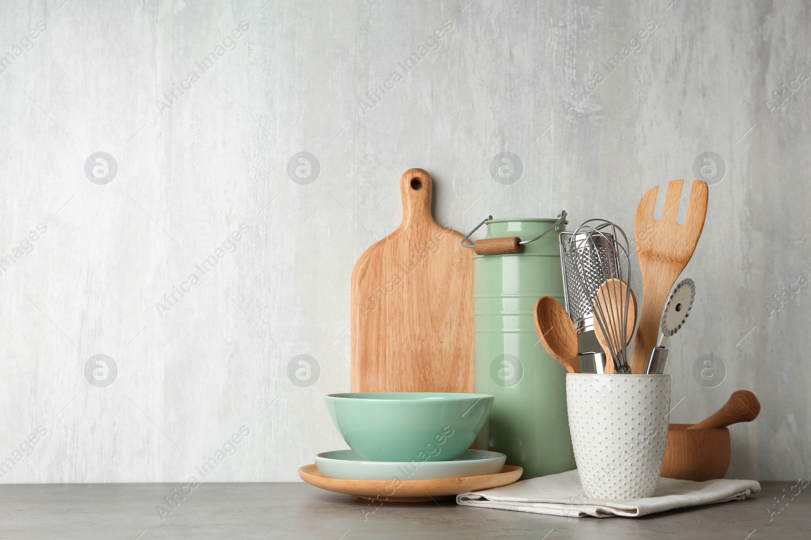 Photo of Different kitchen utensils on grey table against light background. Space for text