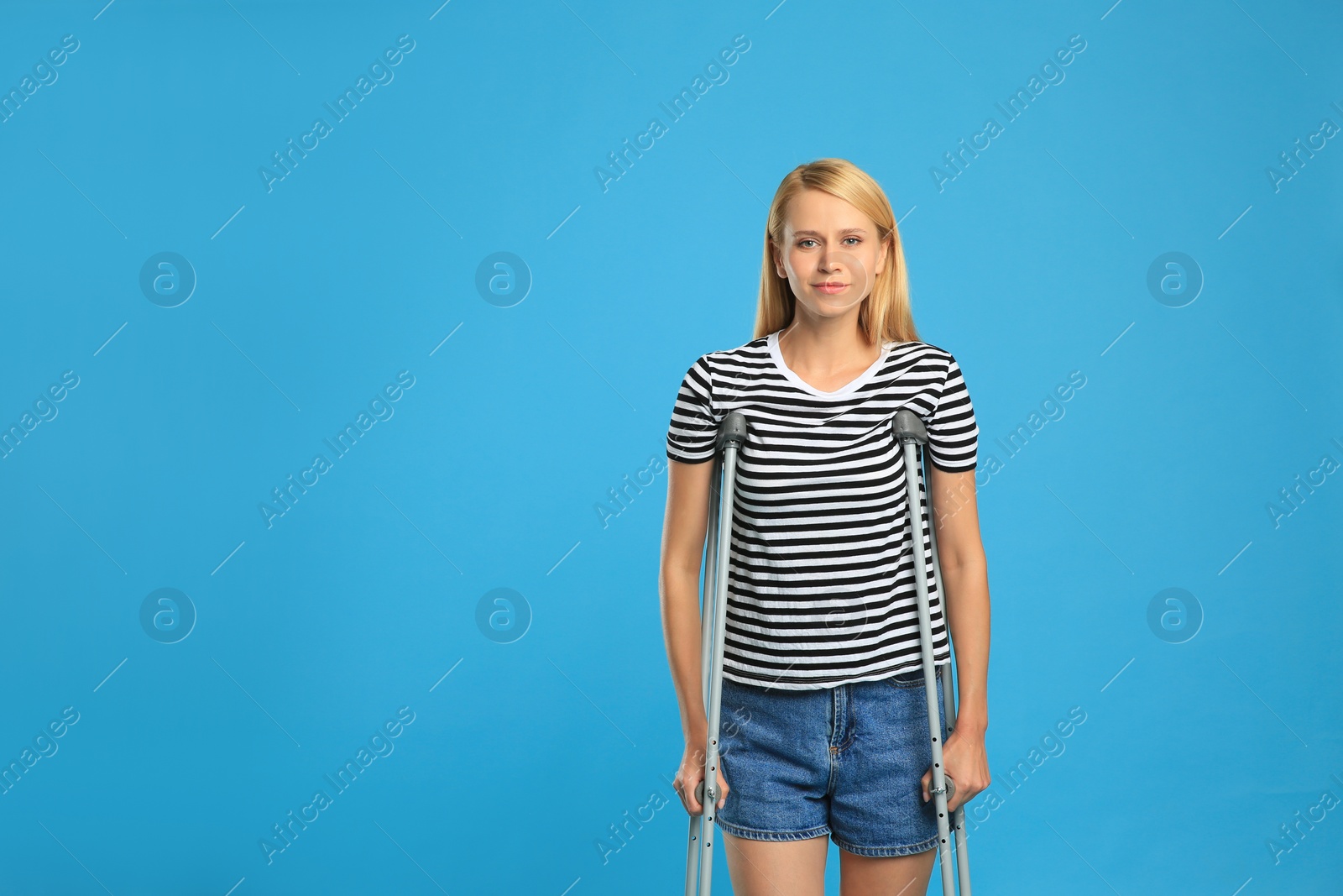 Photo of Young woman with axillary crutches on light blue background, space for text