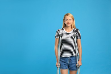 Photo of Young woman with axillary crutches on light blue background, space for text