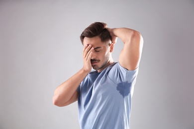 Sweaty man with stain on t-shirt against gray background. Using deodorant