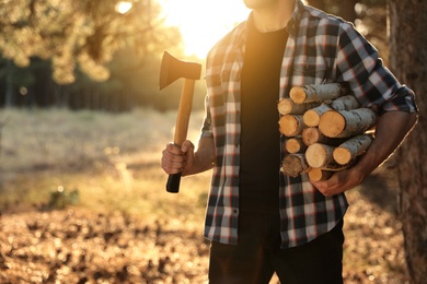 Photo of Man holding pile of cut firewood and axe in forest, closeup