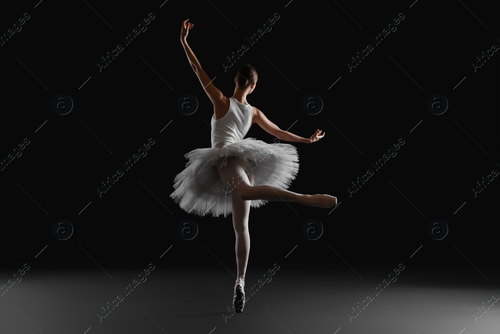 Photo of Young ballerina practicing dance moves on black background