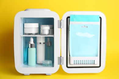 Photo of Open cosmetic refrigerator with skin care products on yellow background