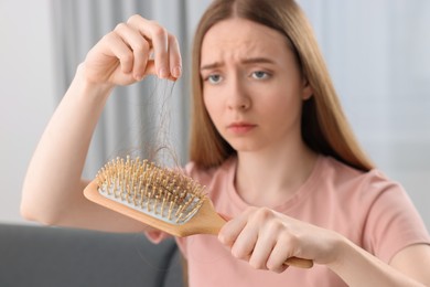 Photo of Woman untangling her lost hair from brush at home, selective focus. Alopecia problem