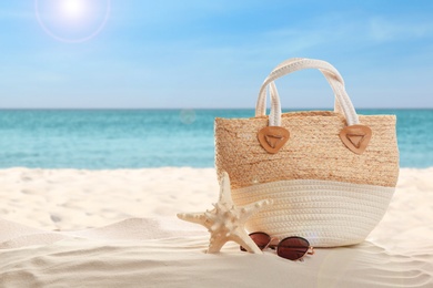 Bag and stylish glasses on sand near ocean, space for text. Beach accessories