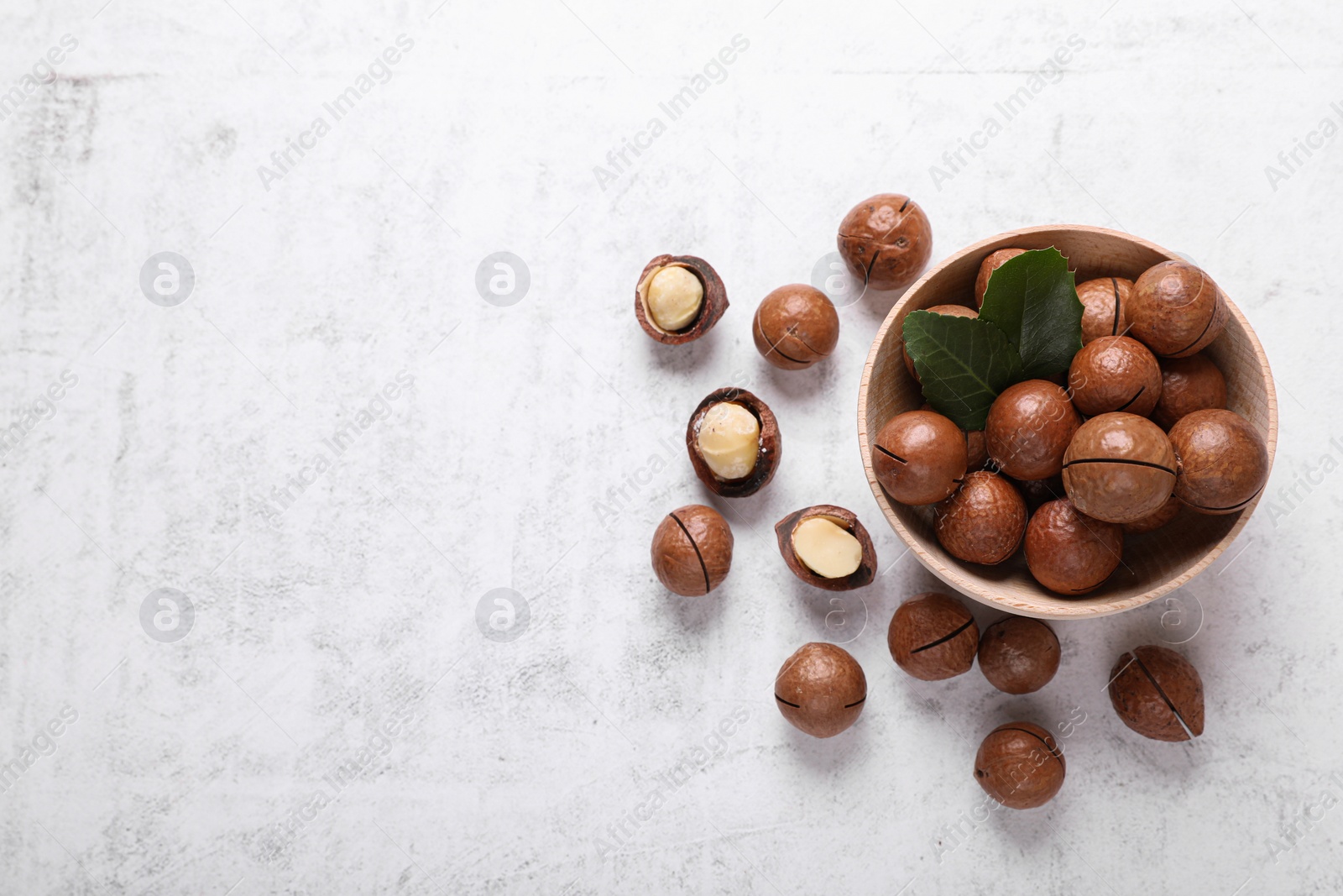 Photo of Delicious organic Macadamia nuts on white textured table, flat lay. Space for text