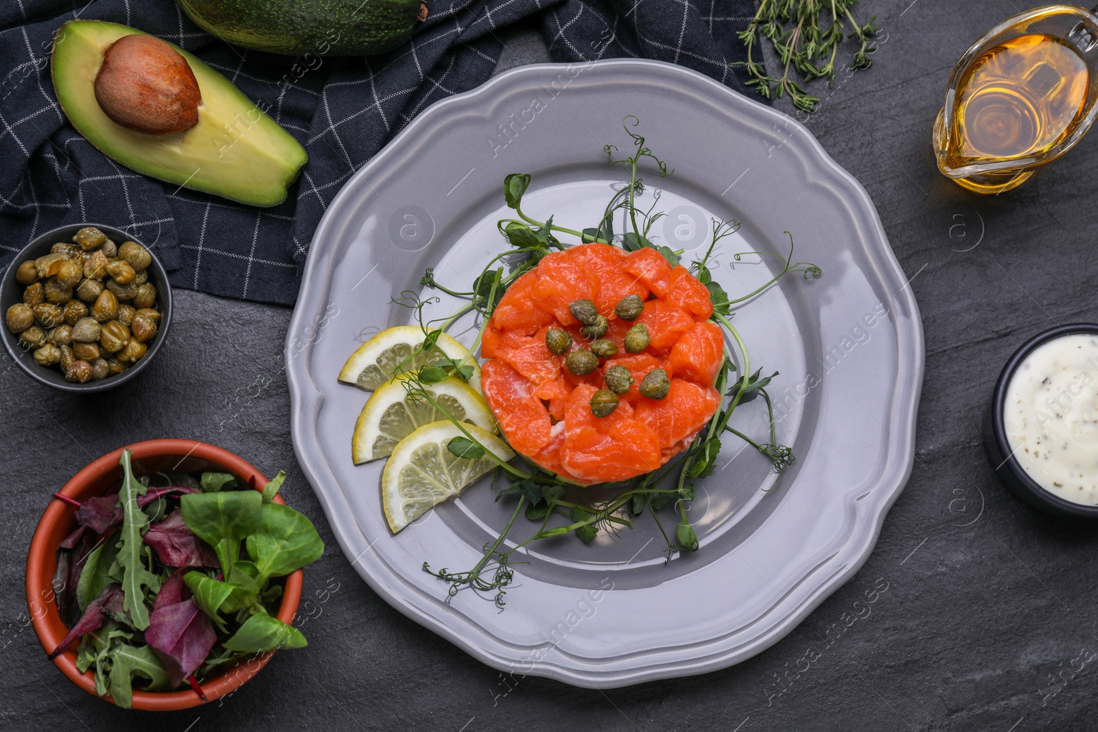 Photo of Delicious salmon tartare with microgreens and lemon on dark table, flat lay