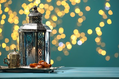 Traditional Arabic lantern, dates and vintage cup holder on table against dark turquoise background with blurred lights. Space for text