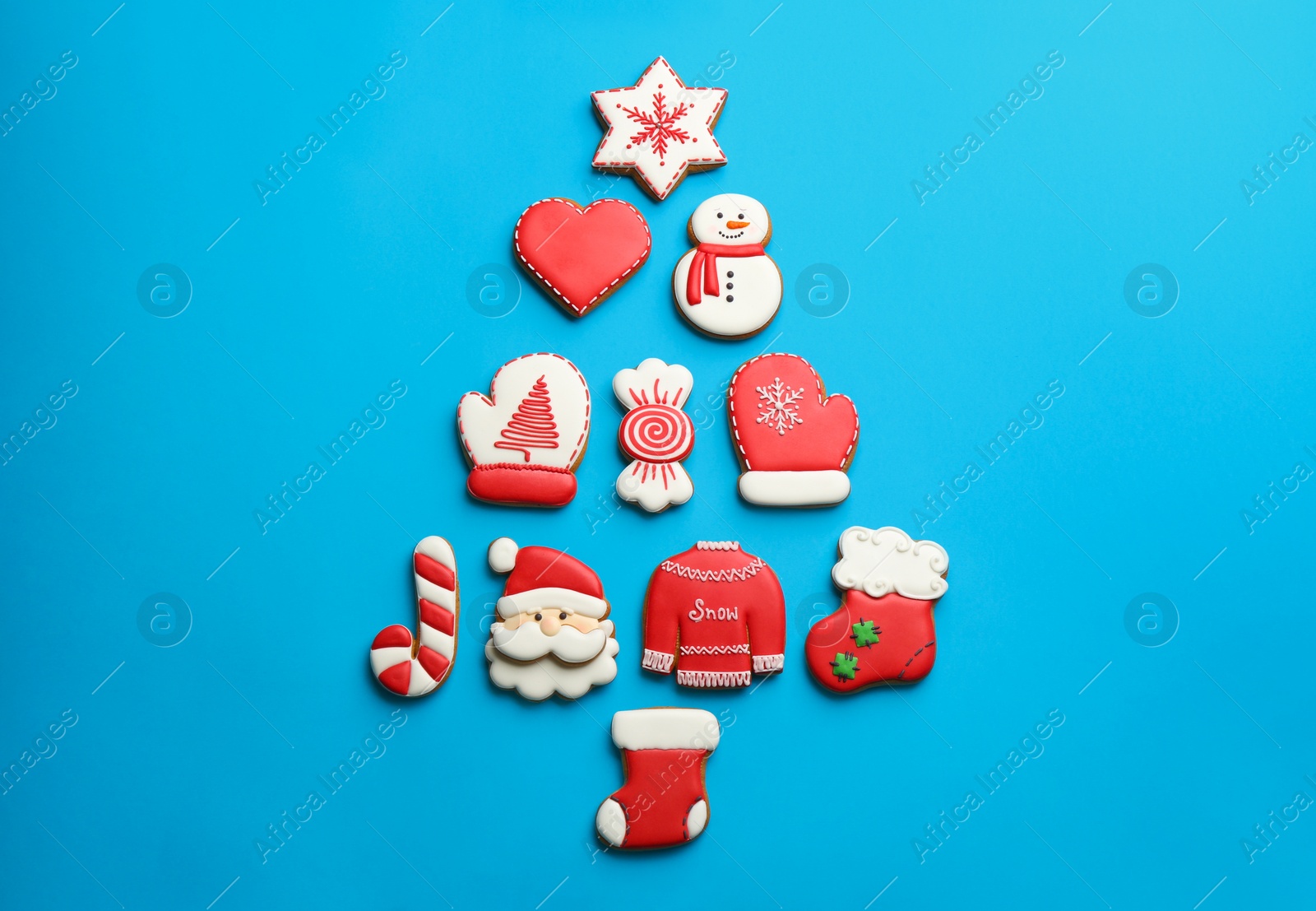 Photo of Delicious gingerbread cookies arranged in shape of Christmas tree on light blue background, flat lay